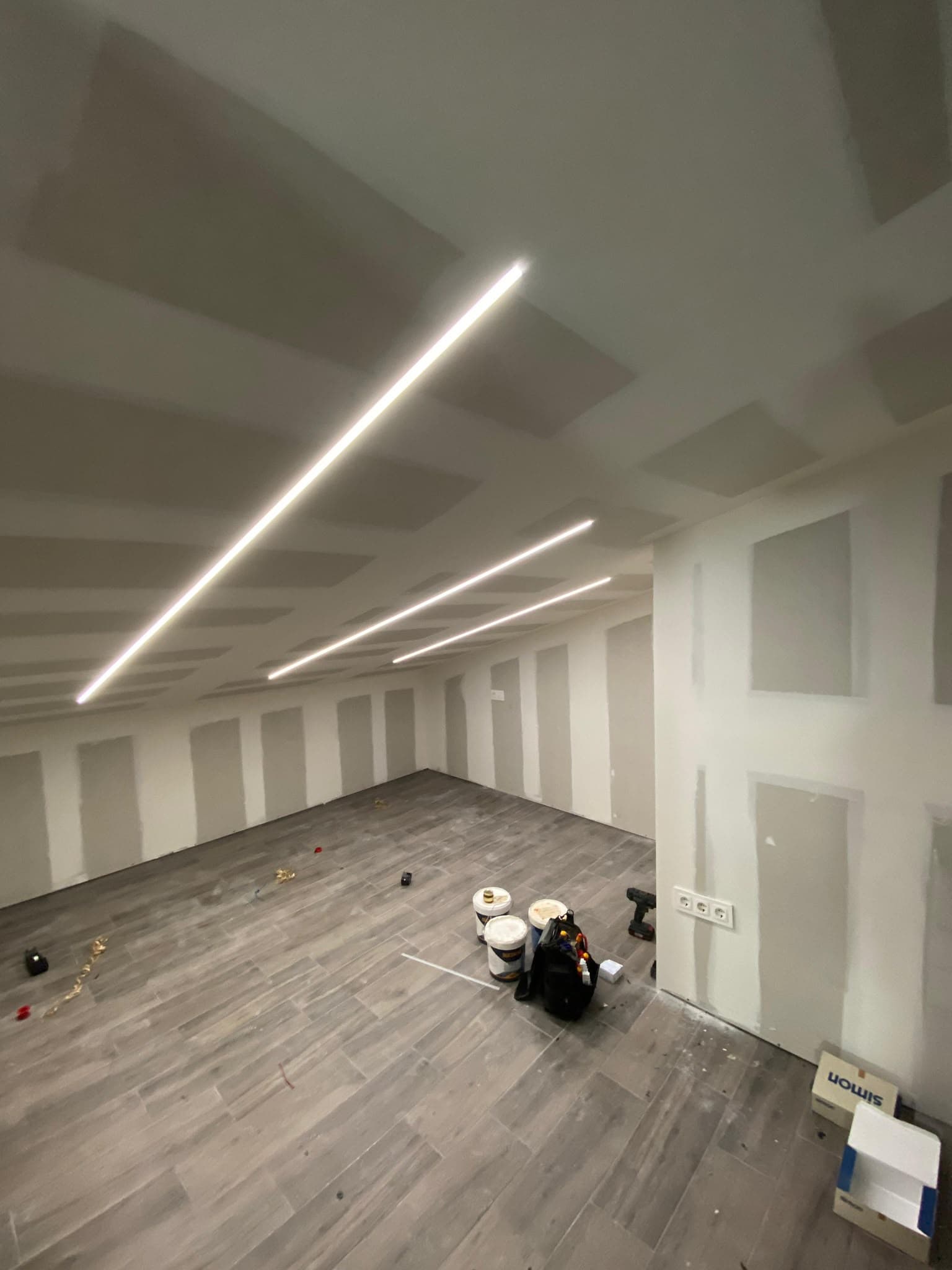 Estancia abuhardillada en obra, con paredes sin pintar y tiras LED ya instaladas
