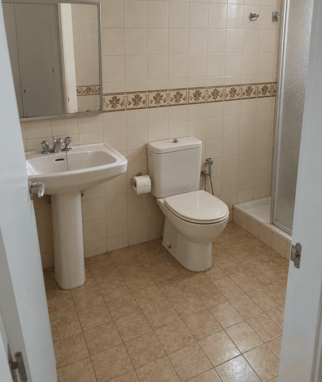 Baño antiguo con lavabo sobre pie y azulejo con cenefa floral, antes de la reforma