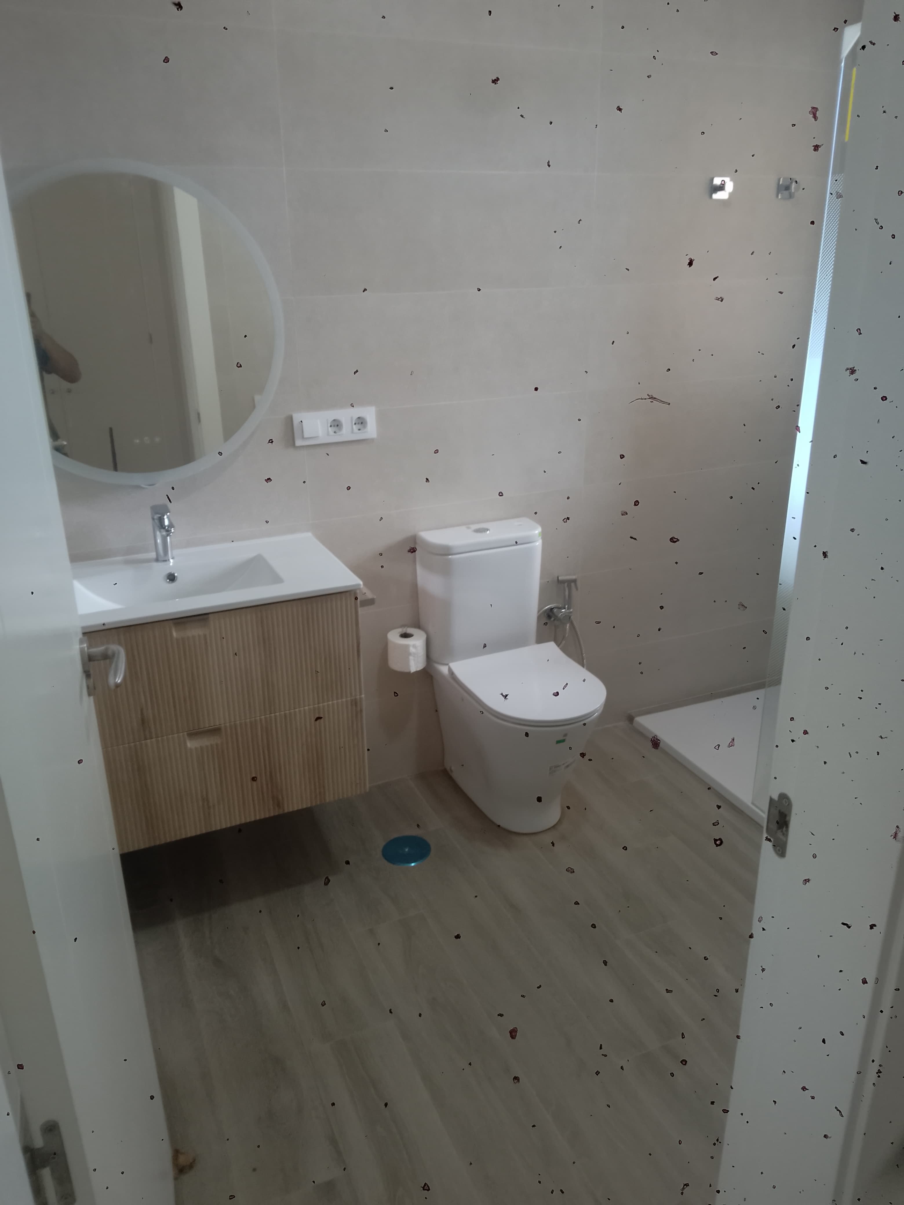 Baño terminado con mueble de lavabo suspendido, espejo redondo y mampara de ducha