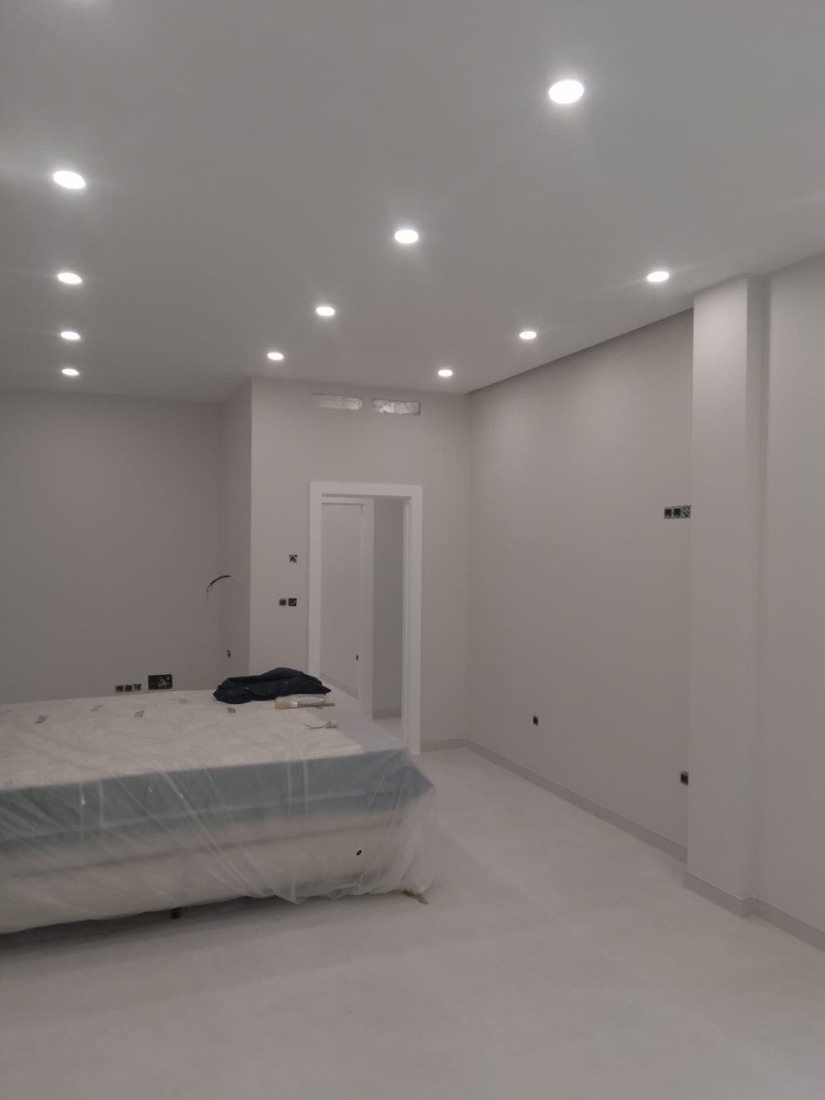 Dormitorio con el techo ya terminado y focos empotrados, con el colchón protegido con plástico mientras continúan los acabados