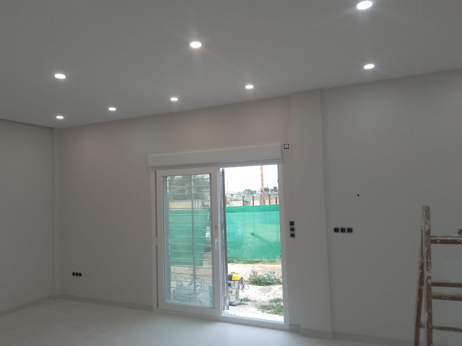 Habitación con el techo terminado y focos empotrados, con la puerta corredera abierta hacia un exterior todavía en obras