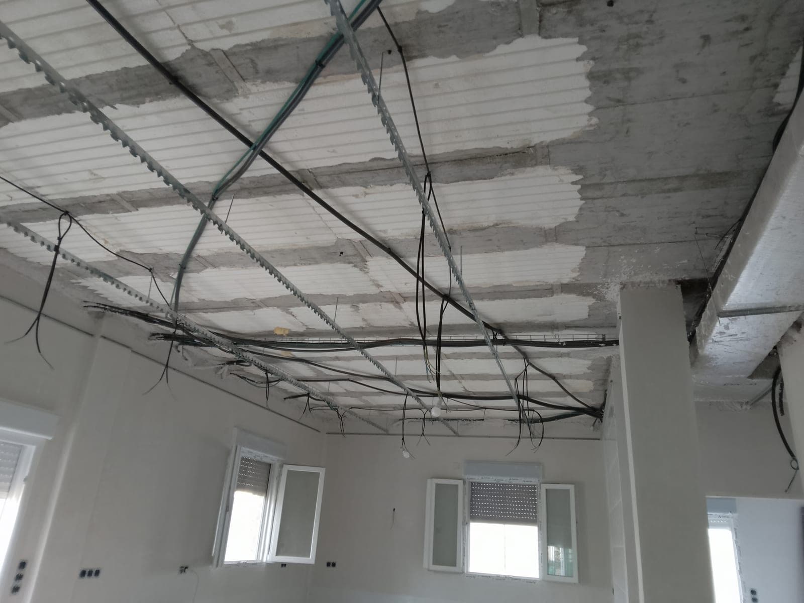 Perfiles metálicos del techo con cableado eléctrico cruzado y aislamiento del forjado todavía visible entre las canaletas