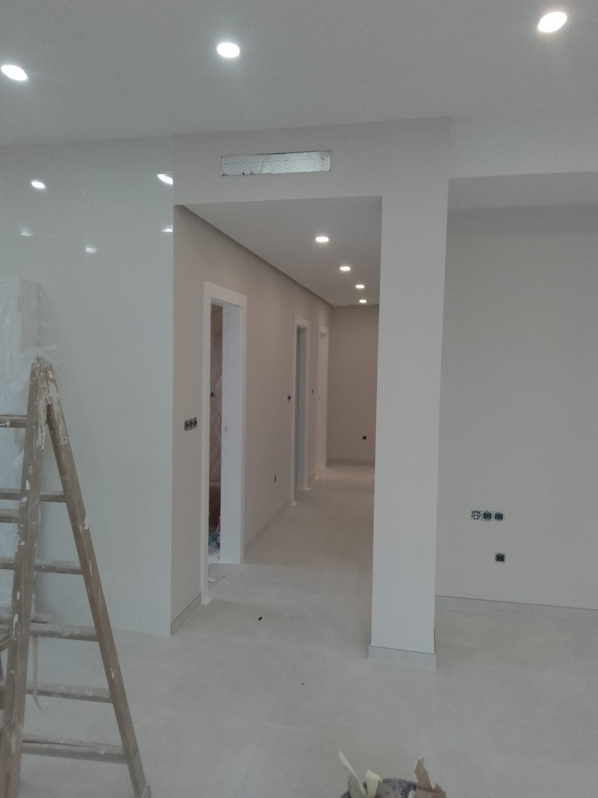 Pasillo con el techo terminado y focos empotrados, sin falseado perimetral, con una rejilla de aire acondicionado sobre el umbral