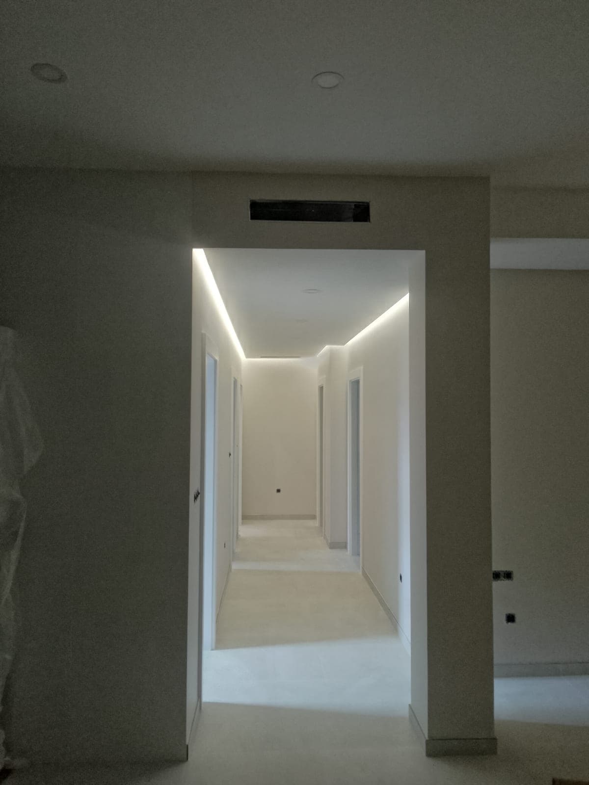 Pasillo con la iluminación led indirecta del falseado perimetral encendida a ambos lados, convergiendo junto a la rejilla del conducto de aire