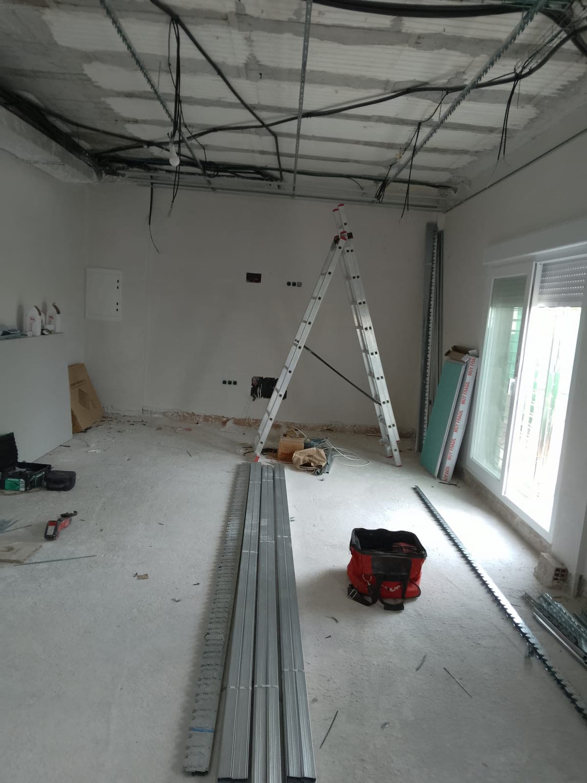 Perfiles metálicos y placas de Pladur acopiados en el suelo de una habitación, listos para empezar el montaje del falso techo